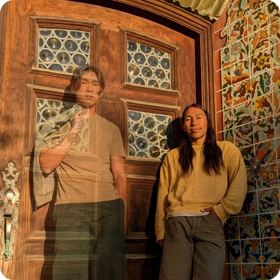 Two people posing in front of a door, the person on the left appears translucent