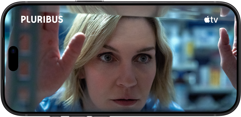 iPhone 18 Pro, landscape mode, displaying a close-up of a woman looking through shelves. Series title: Pluribus