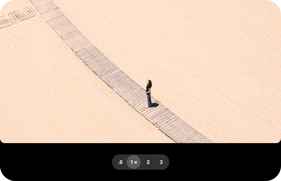 A woman standing on a beach walkway, with a standard 1x zoom.